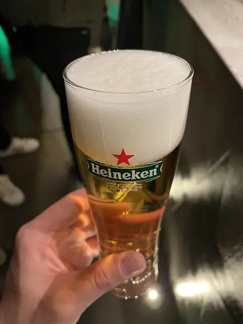 A hand holding a glass of beer with a foamy head.