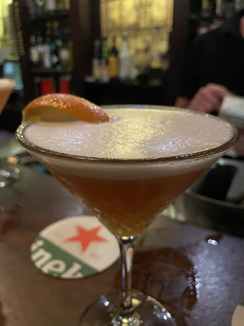 A cocktail garnished with orange peel on a bar table.
