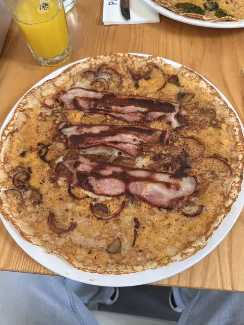 A savory pancake topped with sliced meat on a restaurant table.