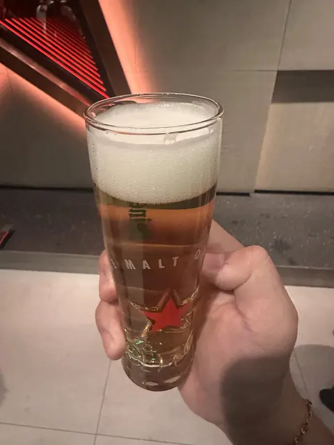 A hand holding a tall glass of beer indoors.