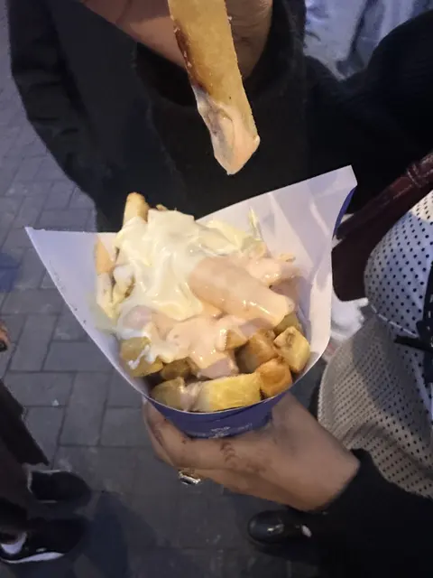 A cone of fries covered with sauce.