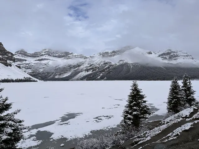 A frozen lake framed by snowy mountains and evergreen trees.