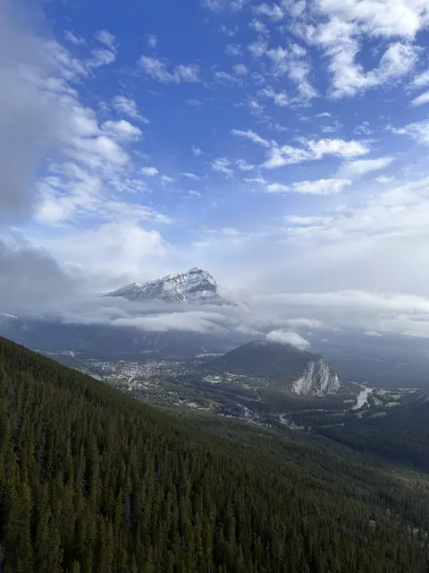 A forested mountain valley beneath clouds and blue sky.