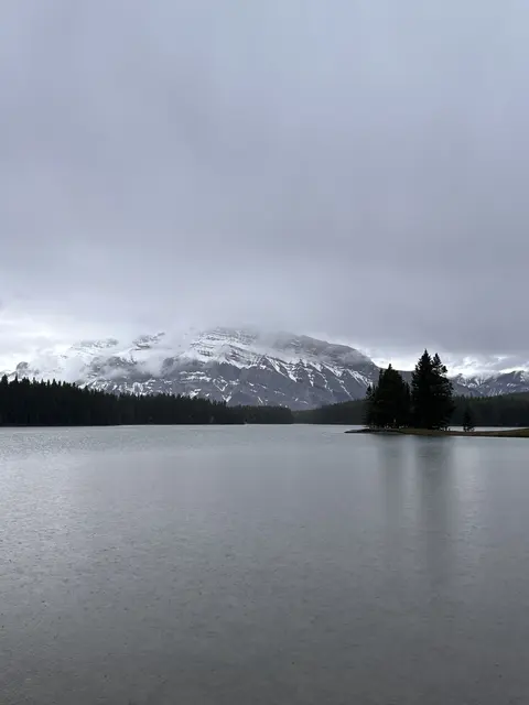 A small wooded island in a lake beneath a grey sky.