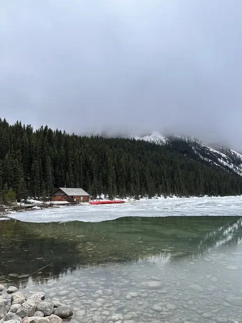A snowy lakeshore with forest and a small wooden building.