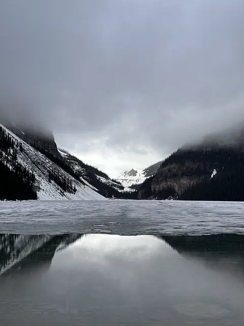 Mountains reflected in open water beside a frozen lake.