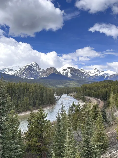 A winding river through evergreen forest beneath snowy mountains.