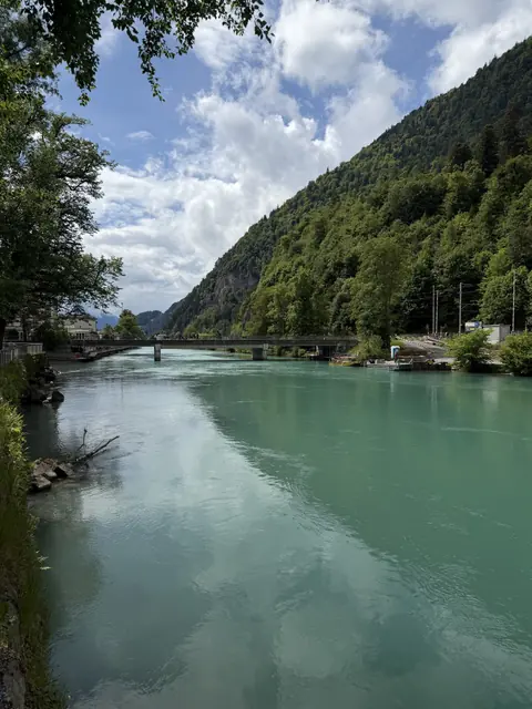 Trees frame a turquoise river and a low bridge.