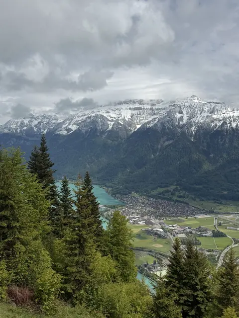 A town, turquoise lake, and fields lie below a snowy mountain ridge.