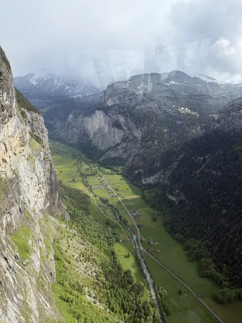 An aerial view of a long green valley between steep cliffs, seen through a window.