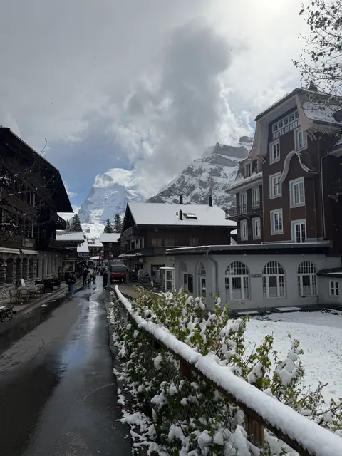 Fresh snow lines a village street beside Hotel Regina with mountains beyond.