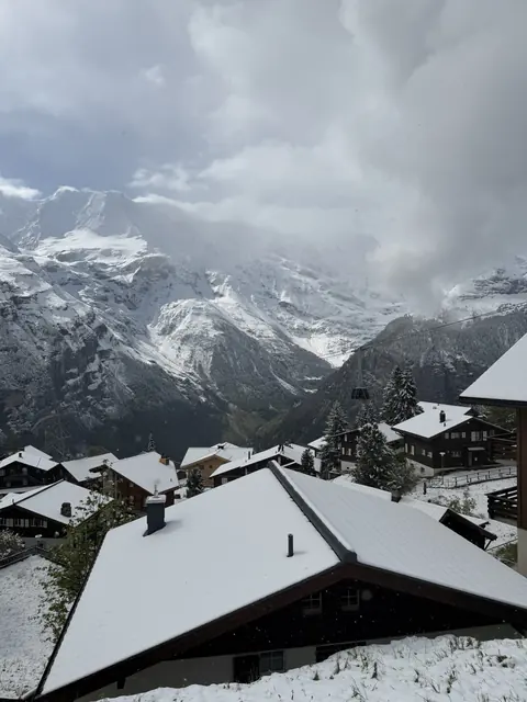 Snow covers chalet roofs below mountains and a cable car.