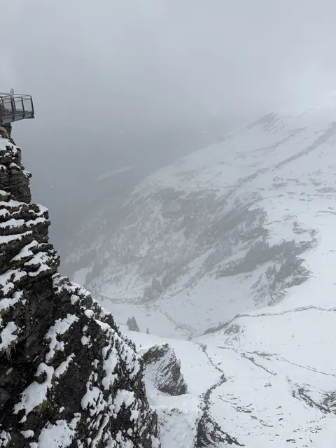 A snowy cliffside lookout overlooks a valley obscured by mist.