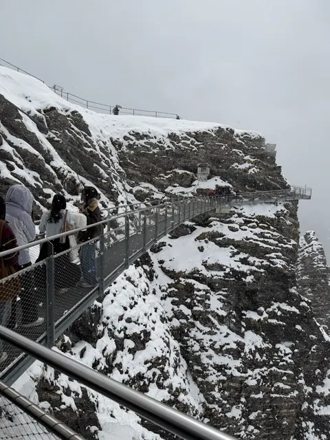Visitors walk along a metal walkway attached to a snow-covered cliff.