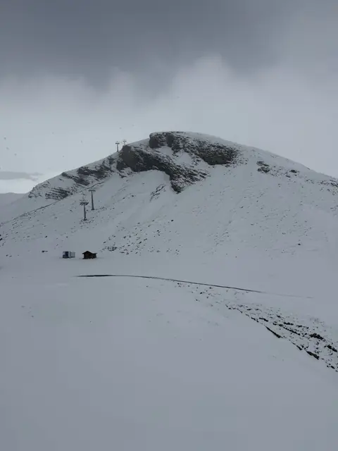Ski lift towers climb a rounded snowy ridge under a grey sky.