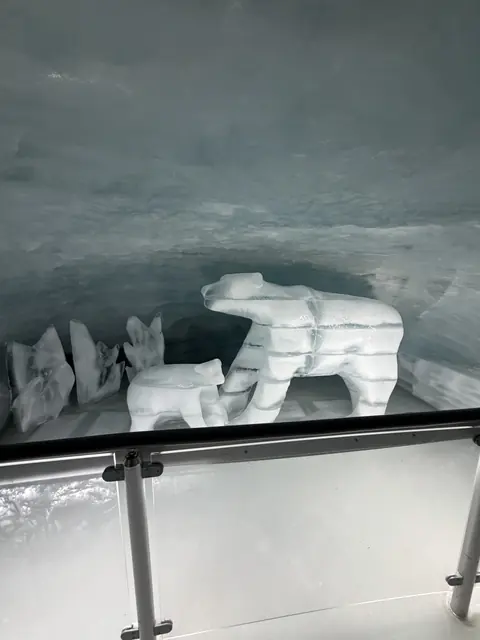 An adult bear and cub carved from ice stand in a frozen chamber.