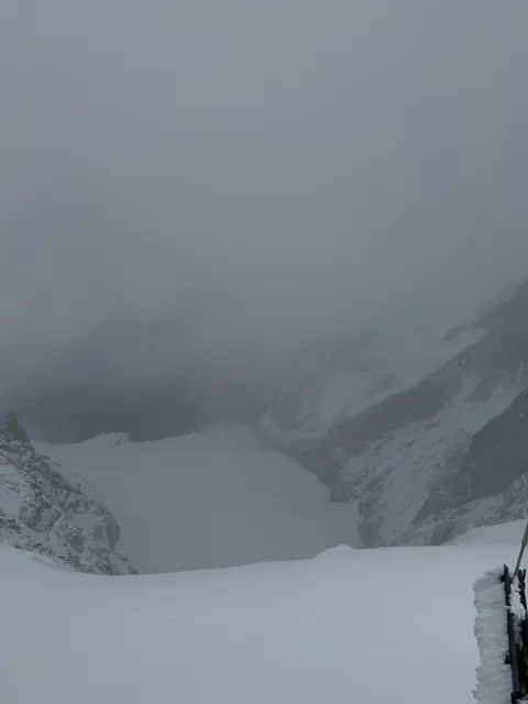 Snow-covered mountain slopes disappear into a thick bank of cloud.