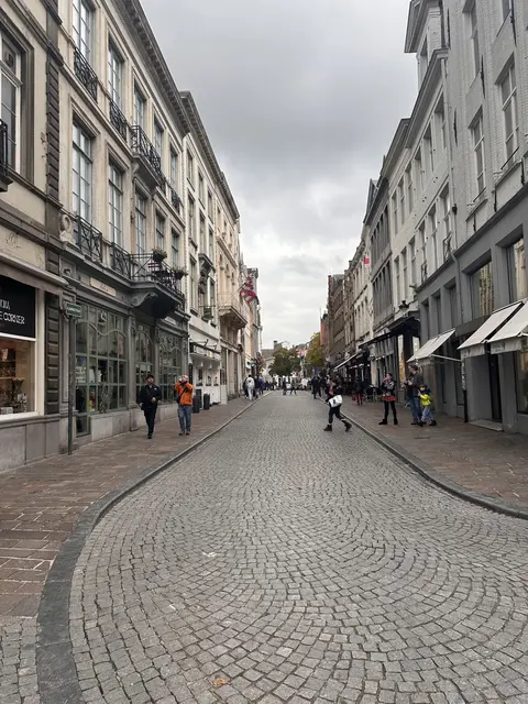 Pedestrians on a cobbled shopping street beneath grey clouds.