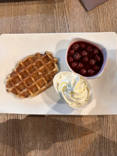 A waffle served with cream and a bowl of cherries.