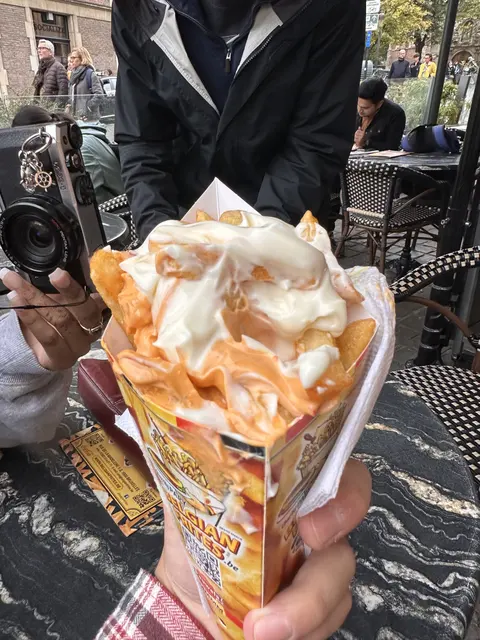 A cone of fries covered with sauce at an outdoor table.