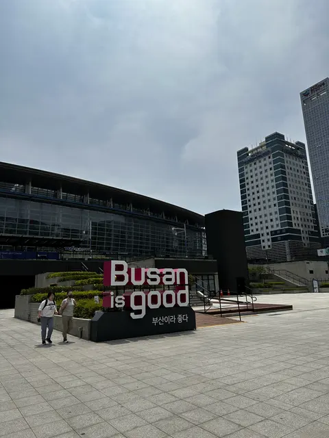 A Busan sign in a plaza outside modern buildings.