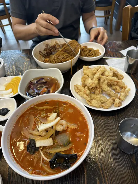Bowls of noodles, fried food, and side dishes on a restaurant table.