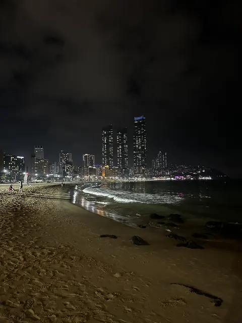 Waves on a beach beside city lights at night.
