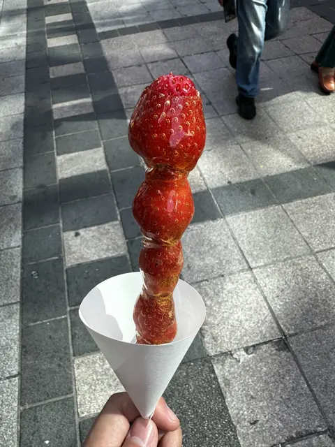 Glazed strawberries on a skewer held above a sidewalk.