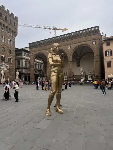 A golden sculpture in a piazza beside an arched loggia.