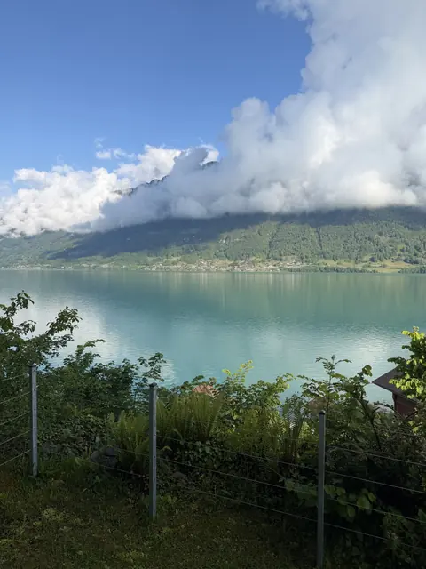 A band of white clouds drifts across a green mountainside reflected in calm lake water.
