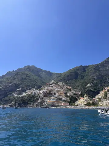 Mountains and seaside buildings above blue water.