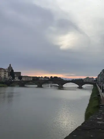 A bridge and buildings reflected in the river at dusk.