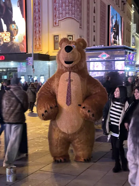 A large costumed bear among people at night.