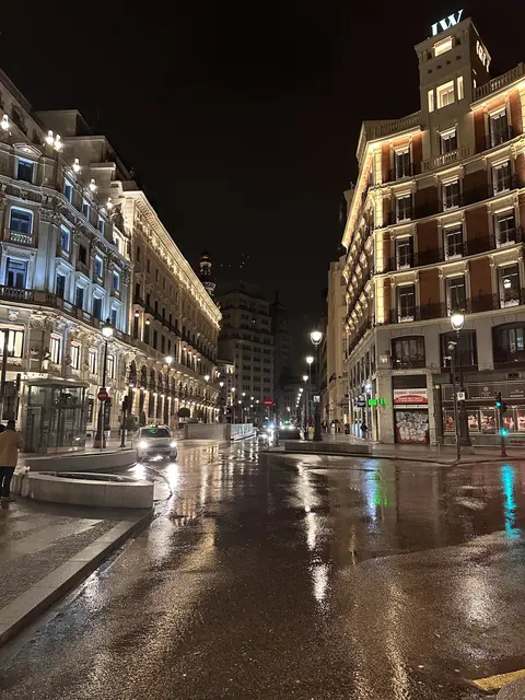 Illuminated buildings reflected on a wet city street at night.