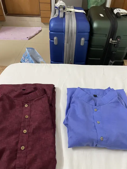 Two folded garments on a bed beside suitcases.