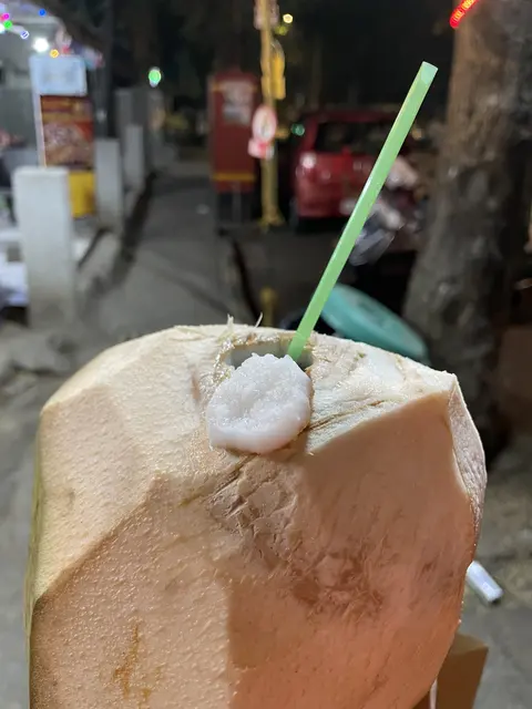 A fresh coconut with a straw on a city street.