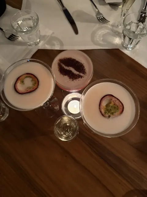 Three frothy cocktails, two topped with passion fruit, around a candle on a table.