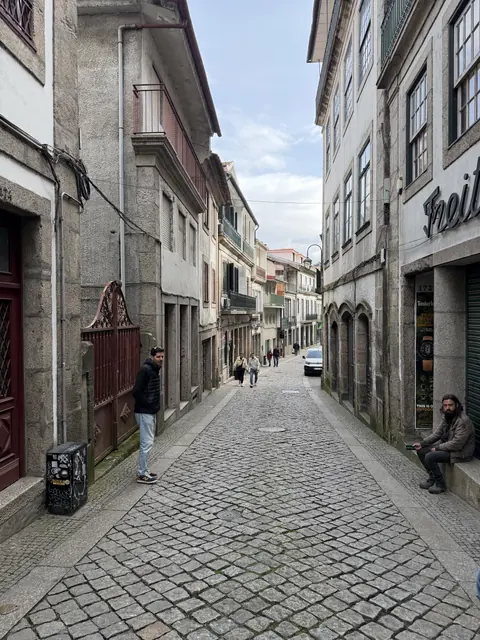 A narrow cobbled street between stone buildings with balconies and pedestrians.