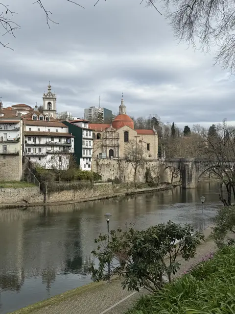 A riverside church, red-tiled roofs, and a stone arch bridge under grey clouds.