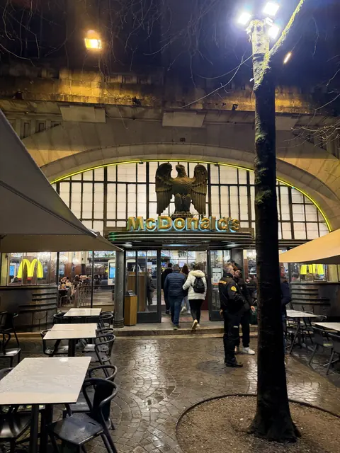 An illuminated McDonald’s entrance beneath an eagle sculpture at night.