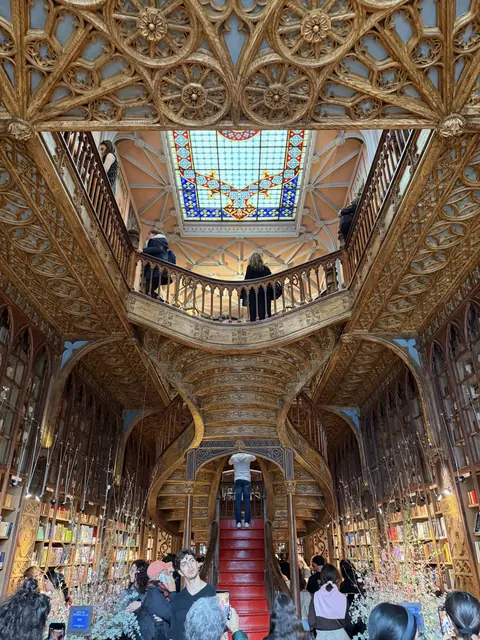 An ornate bookshop with a sweeping red staircase, carved woodwork, and a stained-glass skylight.