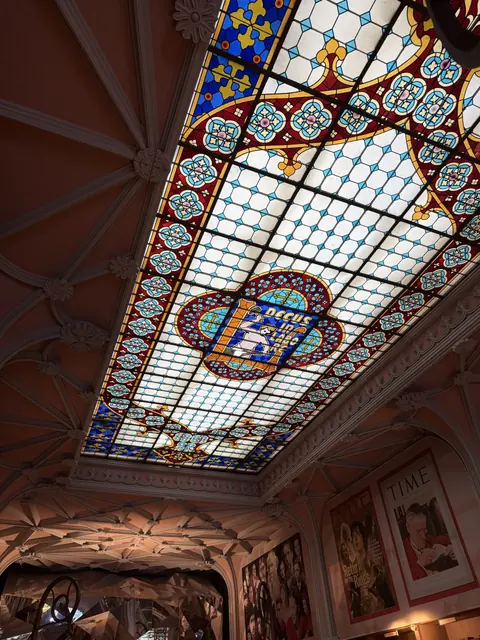 A colorful stained-glass ceiling bordered by decorative plasterwork inside a bookshop.