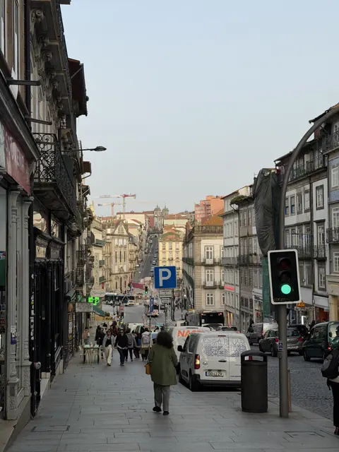 A sloping city street filled with pedestrians and traffic between historic buildings.