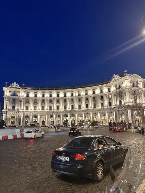 An illuminated curved building overlooking a square at night.