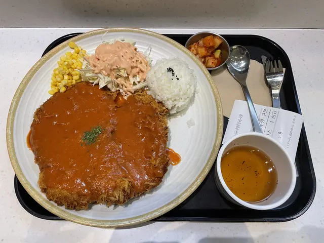 A breaded cutlet with sauce, rice, and side dishes.