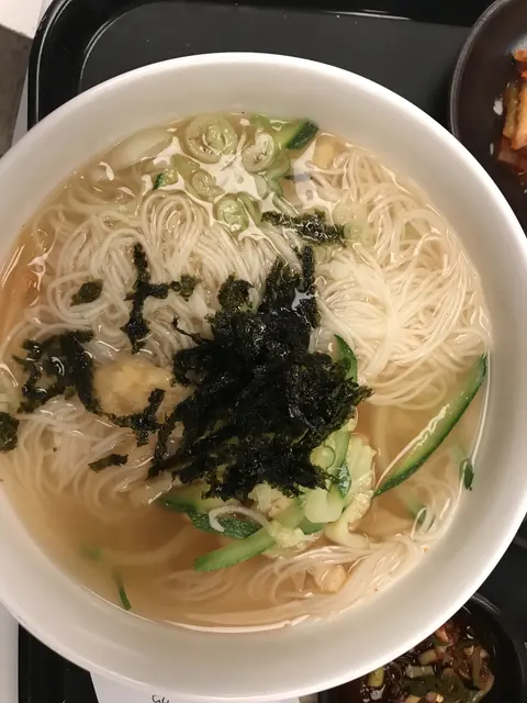 A bowl of noodle soup topped with seaweed and greens.