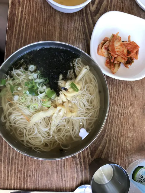 A bowl of noodle soup served with kimchi and tea.