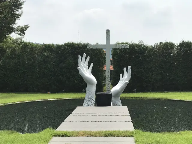 White sculpted hands surrounding a cross in a garden.