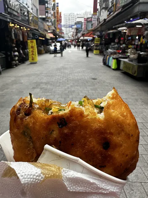 A filled fried snack held in front of a market street.