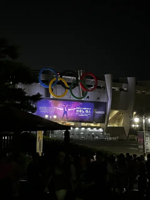 Olympic rings above an illuminated venue at night.